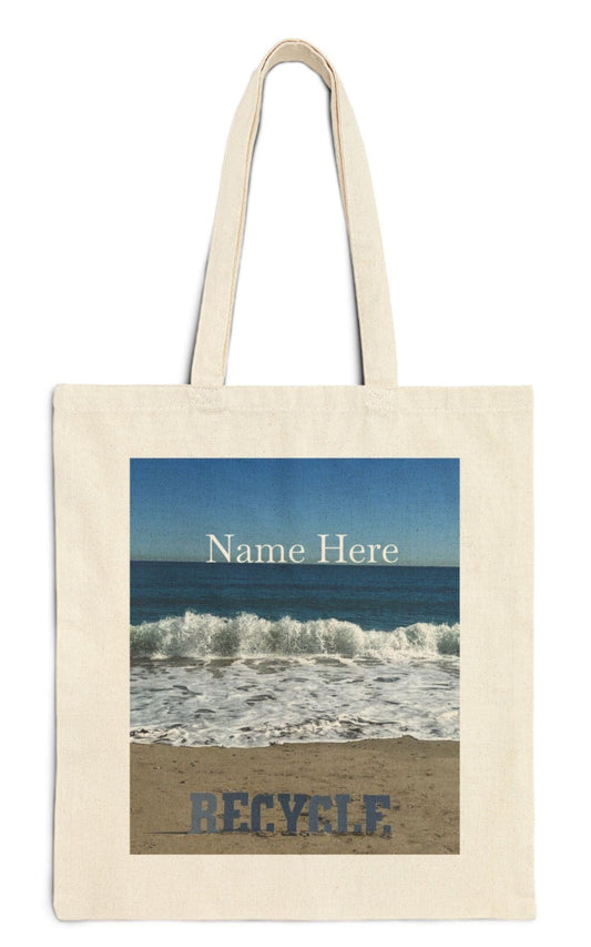 personalized recycle tote bag in natural color the recycle letters are on a sandy shore backed by waves from a blue sea with a blue sky backdrop.