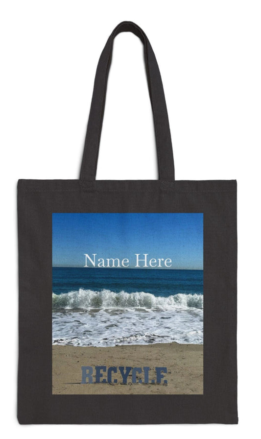 recycle tote bag in black the letters on a sandy beach with waves blue sea and sky